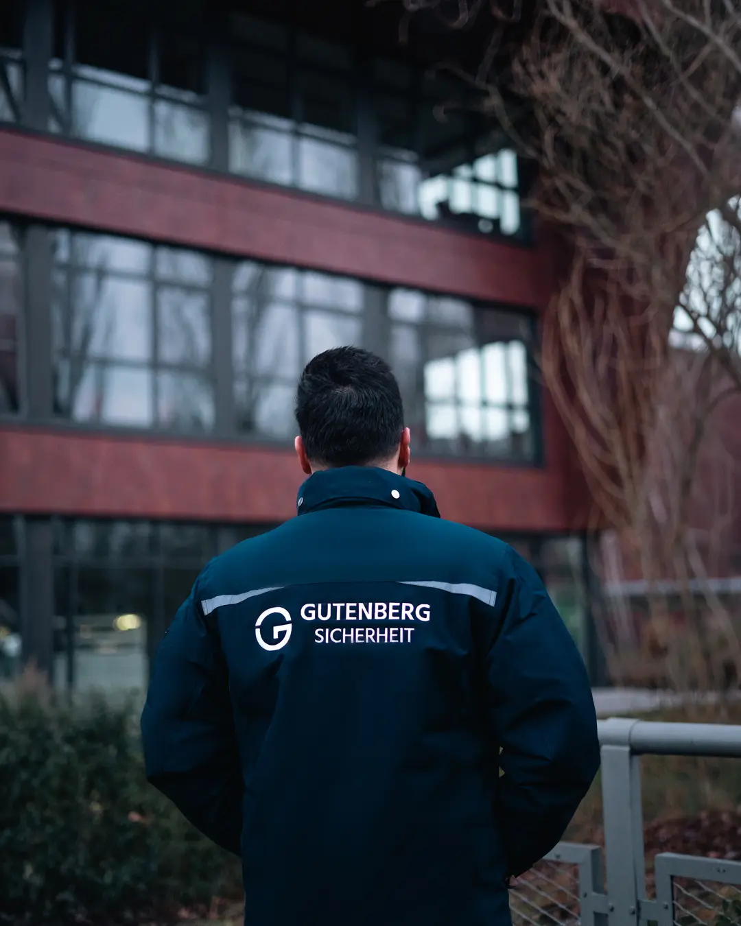Mann mit schwarzer Jacke von Gutenberg Sicherheit steht vor einem modernen Geb&auml;ude.